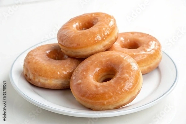 Fototapeta A small stack of glazed donuts resting on a white porcelain plate