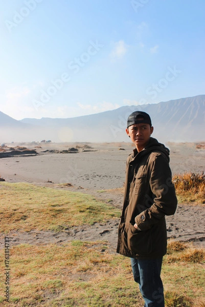 Fototapeta Young Male Traveler Standing Alone in Vast Arid Volcanic Landscape. Conveying solitude, exploration, and the feeling of being small in a vast environment.