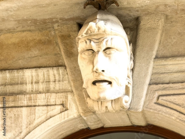 Obraz Trieste, Italy - October 14, 2025: Architectural detail of a historic stone face sculpture above a doorway, showcasing intricate craftsmanship and cultural heritage in an urban setting