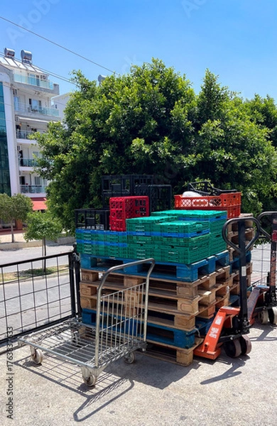 Fototapeta A product cart with stacked pallets and mesh containers filled with fruits and vegetables 