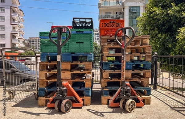 Fototapeta Product carts and pallets stacked with mesh containers at an outdoor market. 