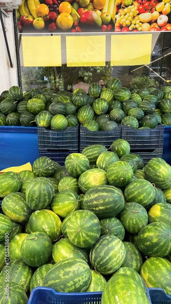 Fototapeta A vibrant street market scene with numerous watermelons stacked in blue containers. Fresh fruits 