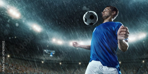 Fototapeta Soccer player performs an action play and beats the ball on a professional rainy stadium. Player wears unbranded sport uniform.