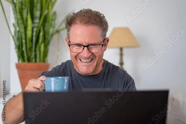 Fototapeta Happy adult man working from home using laptop