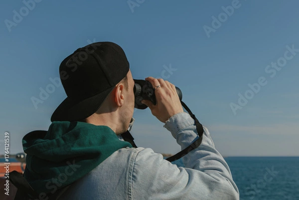 Fototapeta Man looking through binoculars at the sea on a sunny day
