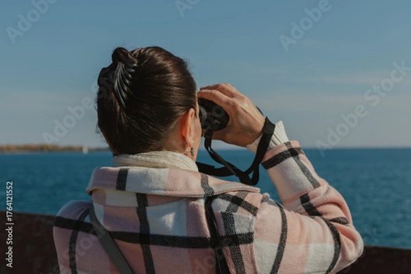 Fototapeta Woman looking through binoculars at the sea on a clear day