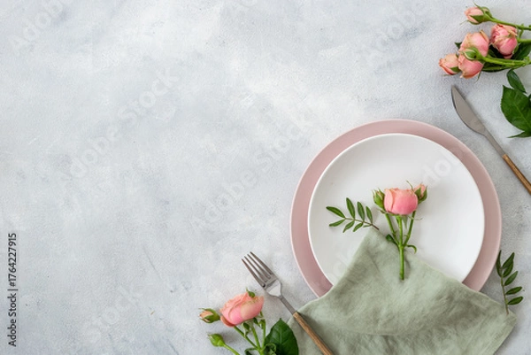 Fototapeta Stylish table setting with empty plate, cutlery and napkin - pink roses flowers decorated on gray stone background, top view, flat lay
