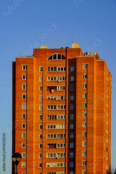 Fototapeta Sunset view of a modern brick apartment building against a clear blue sky in an urban setting