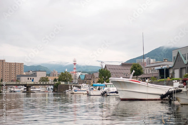 Obraz Fishing boats docked in harbor with city and mountains in background at Hokkaido, Japan
