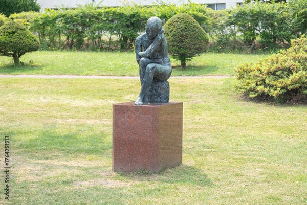 Fototapeta Bronze statue of a seated person in a public park garden at Lake Toya, Abuta, Hokkaido, Japan