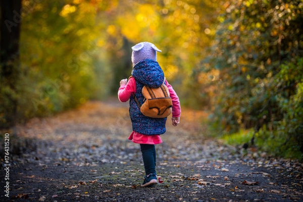 Fototapeta Adorable little girl with cute backpack playing in colorful autumn forest — warm fall tones, active childhood concept, copy space