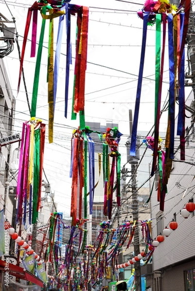 Obraz 商店街の細い通りを縦に覆うように吊るされた色鮮やかでメタリックな輝きを持つ日本の七夕飾りの吹き流しの全景