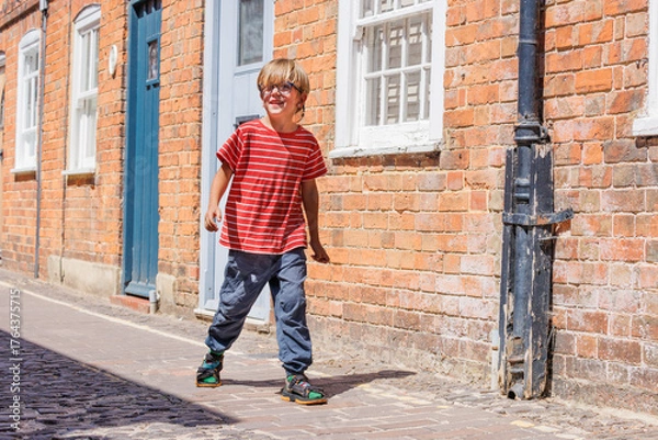 Fototapeta Boy in striped shirt walks joyfully along a sunny brick street