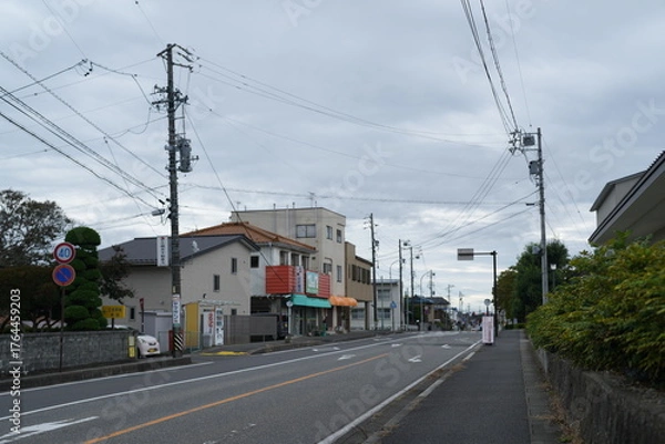 Fototapeta A street with a few buildings and a few cars. The street is empty and the sky is cloudy