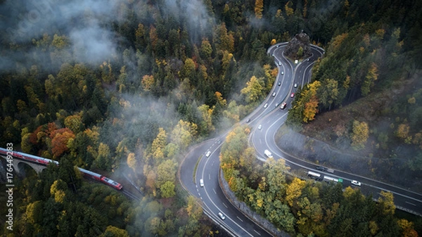 Fototapeta street from above trough a misty forest at autumn, aerial view flying through the clouds with fog and trees