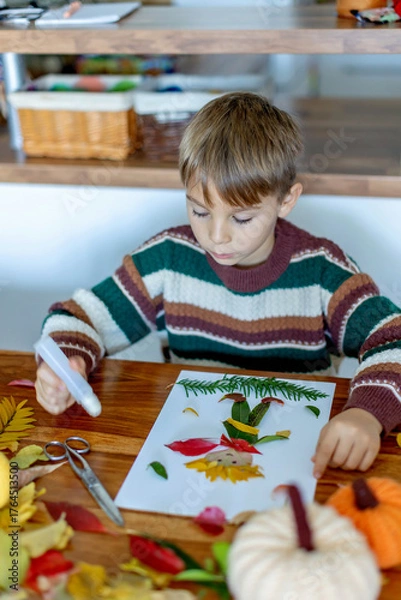 Fototapeta Sweet child, boy, applying leaves using glue while doing arts and crafts at home