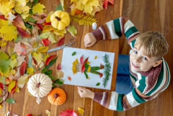 Fototapeta Sweet child, boy, applying leaves using glue while doing arts and crafts at home