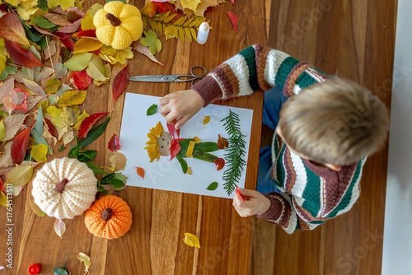 Fototapeta Sweet child, boy, applying leaves using glue while doing arts and crafts at home