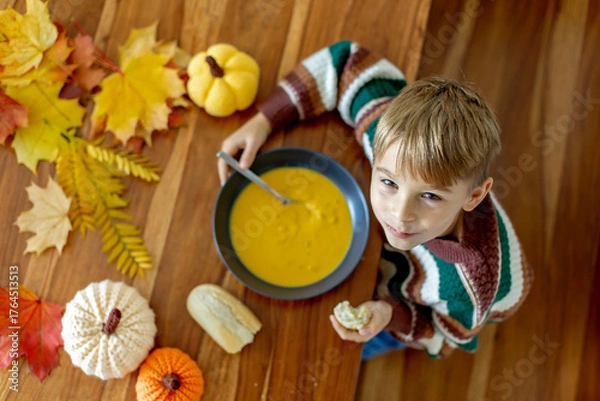 Fototapeta Sweet child, boy, eating pumpkin soup, applying leaves using glue while doing arts and chraft with leaves