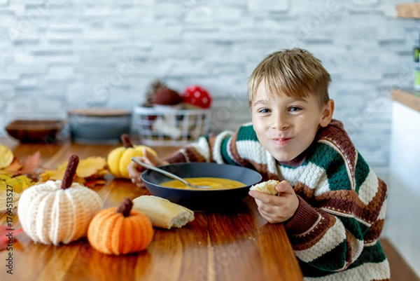 Fototapeta Sweet child, boy, eating pumpkin soup, applying leaves using glue while doing arts and chraft with leaves