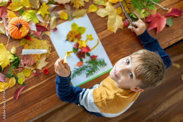 Fototapeta Sweet child, boy, applying leaves using glue while doing arts and crafts at home