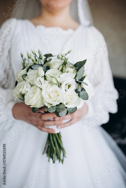Obraz Bride holding a wedding bouquet of white roses and greenery. A tender and elegant image symbolizing purity, harmony, and the beginning of a new happy life.