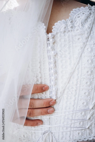Obraz Close-up of a groom gently holding the bride in a white lace wedding dress. Elegant details of buttons and veil. Romantic and tender wedding moment.
