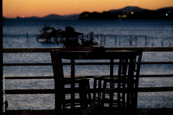 Fototapeta Table and chairs by the sea at sunset with calm evening light