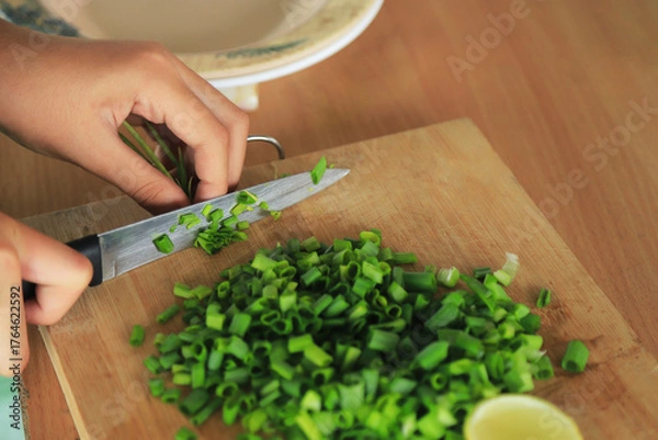 Fototapeta hands cutting green spring onion on cutting board for cooking