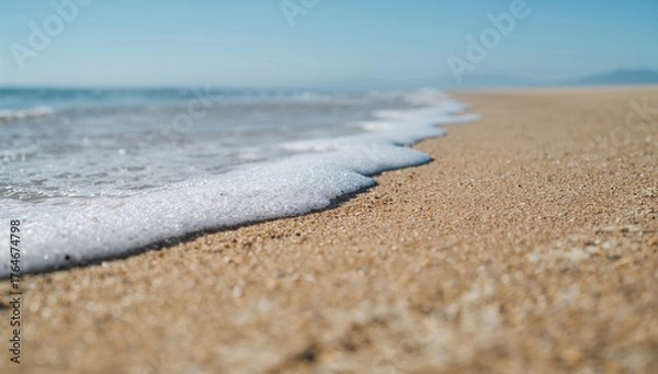 Fototapeta Sunlit sandy shore with gentle waves and empty space