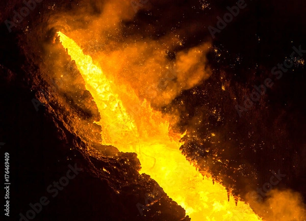 Fototapeta Tapping the blast furnace, liquid molten iron flowing out of the taphole of a blast furnace, lava-like. The iron temperature exceeds 1350 degrees Celsius.