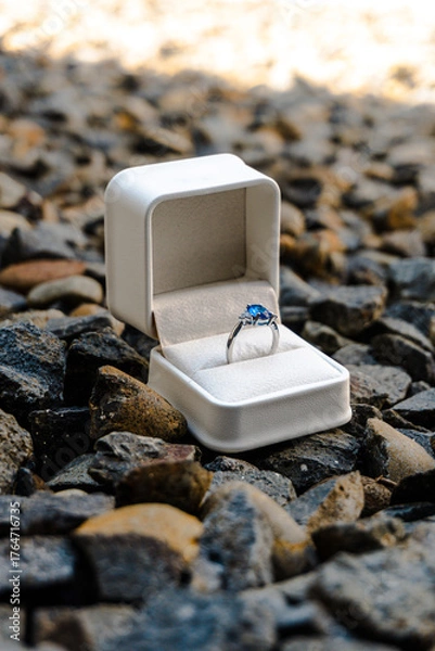 Fototapeta Stunning sapphire engagement ring in a white box placed on rugged dark gravel, symbolizing a bold, outdoor proposal or unique commitment