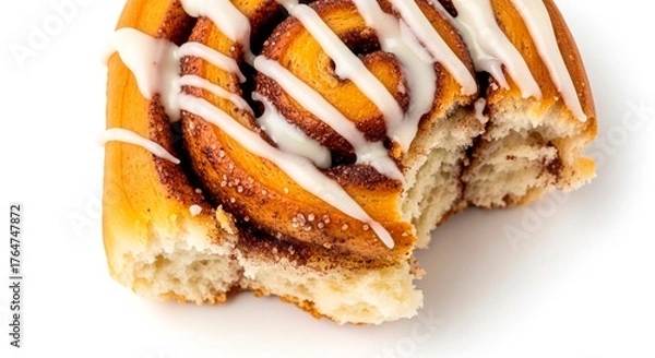 Fototapeta A close up of a partially eaten cinnamon roll with white icing on a white surface in bright lighting