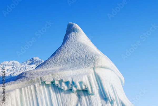Fototapeta Tip detail of a giant blue iceberg against blue sky and cloud background. Kjerulf Fjord, Northeast Greenland National Park. Huge icebergs become stranded here and are weathered into sculptural shapes.