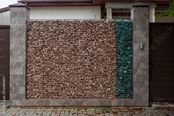 Obraz Gabion wall with brown and green stones between tiled pillars near garage entrance. Design fences, fencing of the homestead plot. Real photo