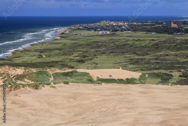 Fototapeta Landscape photo with a view of sand dunes, green hills and the town of Lonstrup in the background near the Rubjerg Knude lighthouse in Denmark