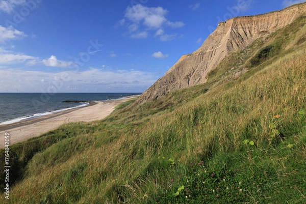 Fototapeta Landscape photo with a view of the North Sea coast, beach and rocky hills against a blue sky with clouds near Bovbjerg Lighthouse in Lemvig, Denmark