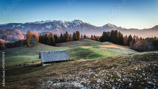 Fototapeta Snow-dusted mountains and a rustic cabin at sunrise.