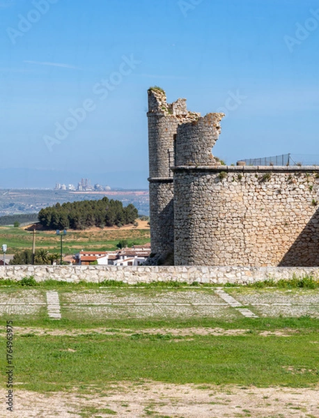 Obraz The medieval stone wall and entrance of the weathered Castillo de los Condes in Chinchón, Spain, framed by a lively field of yellow wildflowers and surrounded by a dirt road