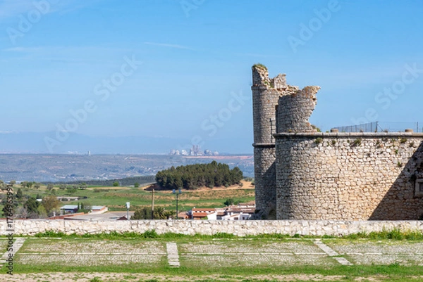 Obraz The medieval stone wall and entrance of the weathered Castillo de los Condes in Chinchón, Spain, framed by a lively field of yellow wildflowers and surrounded by a dirt road