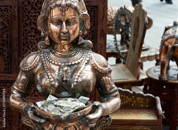 Fototapeta Bronze statue of Indian goddess holding coins and banknotes as offerings, traditional Hindu art sculpture with detailed craftsmanship