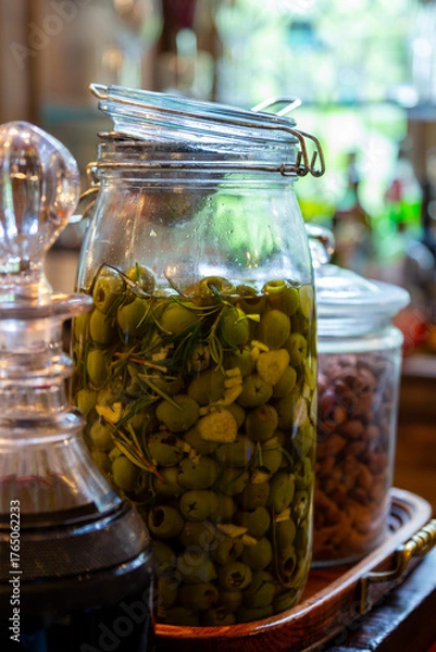 Obraz A large glass jar of green olives marinating in olive oil with sliced garlic and rosemary makes an elegant bar snack. Graphic resource