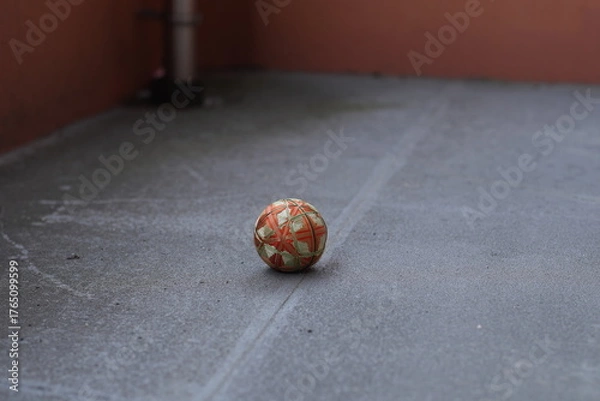 Fototapeta A small orange and green ball is sitting on a grey concrete floor