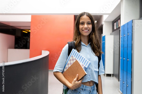 Obraz Smiling student girl holding books in school hallway