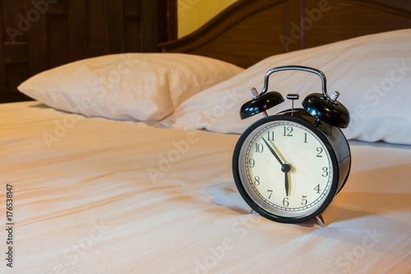 Fototapeta Analog alarm clock is on white bed, time in the morning.