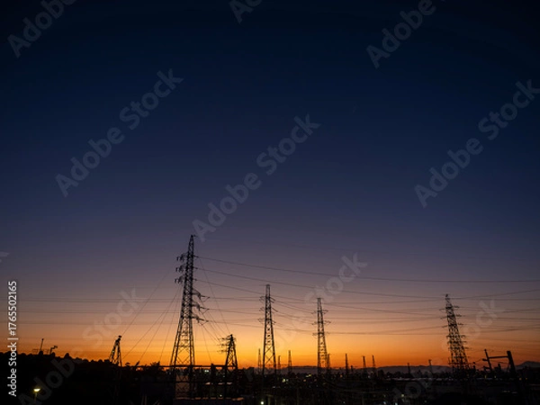 Fototapeta 夕焼け空と都市の風景。街並み。鉄塔と電線。オレンジ色から濃紺へのグラデーションの空。日没。横構図。広いコピースペース