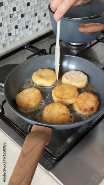 Fototapeta Anonymous person fries potato croquettes in vegetable oil in new, trendy frying pan. Farm produce. Home cooking. Traditional cuisine.