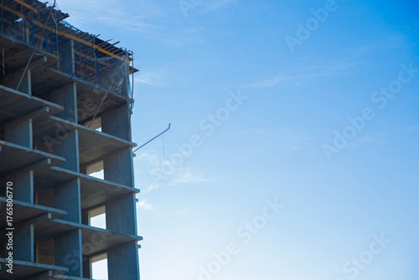 Obraz A partially constructed concrete building on the construction site with scaffolding and a bright blue sky, highlighting architectural progress and development. The concept of construction of an