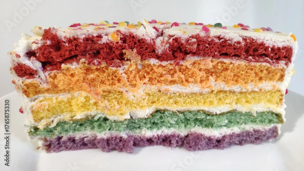 Fototapeta Slice of rainbow layer cake with sprinkles and white frosting 
