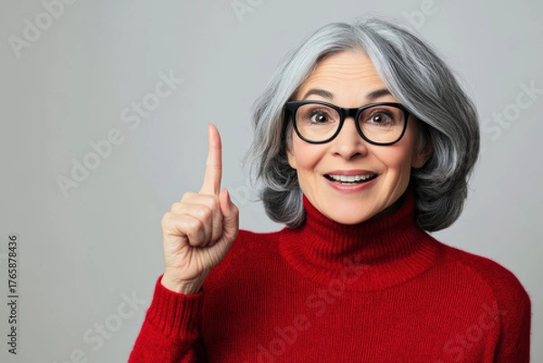 Fototapeta Smiling older woman in red sweater pointing upward with excitement